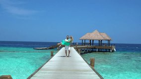 A couple on a wooden pier in the Maldives, with the man carrying the woman, surrounded by clear turquoise water and a thatched-roof structure in the background. - Powered by Shutterstock - Get 15% off with code: PIKWIZARD15