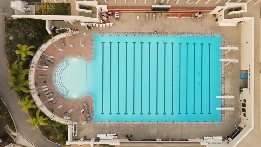 Drone view rising over an outdoor swimming pool next to a college stadium