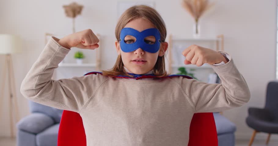 Portrait of cheerful boy in superhero costume playing with fun during leisure at home, showing muscle strength in a domestic environment with focus on joy and strong playful engagement.