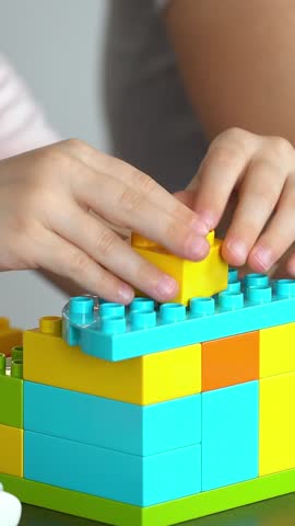 Childs hands build plastic brick of construction set. Girl plays with construction kit. Leisure. Vertical shot