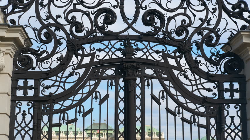 Capturing intricate details of an ornate iron gate adorned with heraldic symbols, set against a vibrant blue sky backdrop. Perfect for historical and architectural themes