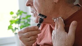 Senior Man shaving his face. Old male shaves beard and mustache with shaver. Elderly gray haired man looking at the mirror, applies shaving cream foam and using razor. Skin hygiene. Daily body care - Powered by Shutterstock - Get 15% off with code: PIKWIZARD15