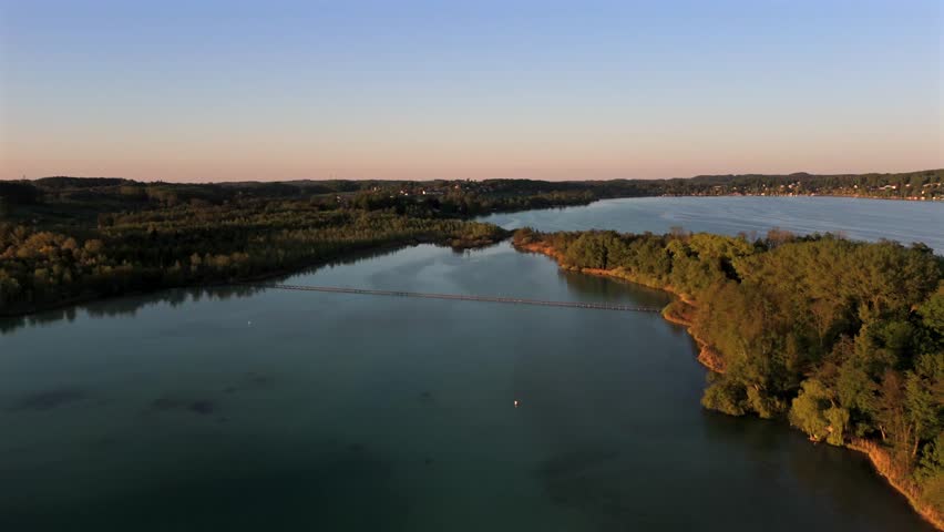 Aerial view of the 260-meter-long wooden causeway bridge to Mausinsel, a private island on Lake Woerthsee, Bavaria, Germany. Surrounded by forest, calm water, and scenic summer beauty