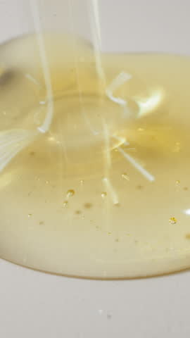 Drops of fresh jojoba oil falling down spreading on white plain surface. Transparent golden liquid with small bubbles. Skincare product macro
