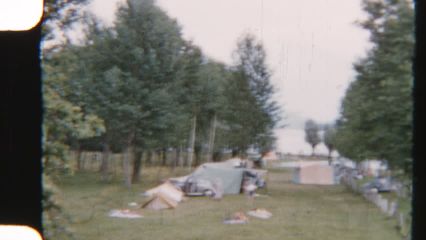 8mm footage of a family setting up tents on the serene shores of Lake Como, creating a cozy campsite with a picturesque backdrop of the tranquil waterfront