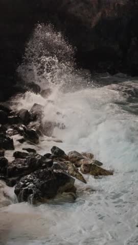 A dynamic seascape shows waves crashing against rugged rocks, creating splashes and foam everywhere.