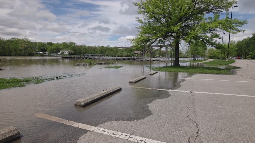 Sunny day of flooded parking lot full of river water by boat ramp, causing a flood to overflow park spots for vehicles from recent rainfall and rainy weather in slow motion
