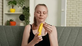 Healthy food advertisement concept. Young woman sitting on sofa at home and eating fresh vitamin fruit, peeling off and biting ripe banana, chewing and smiling, enjoying snack. Slow motion. - Powered by Shutterstock - Get 15% off with code: PIKWIZARD15