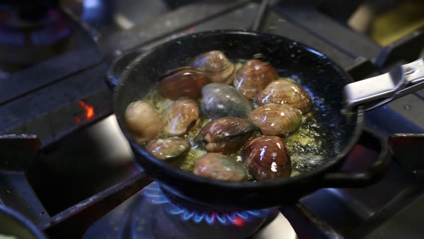 Sauteing fresh clams and garlic over gas flame, sizzling in professional restaurant kitchen, showcasing culinary preparation