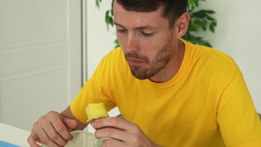 Healthy food advertisement concept. Young man sitting at the table at home and eating fresh vitamin veggies, biting boiled potato, chewing and nodding, enjoying snack. Slow motion.