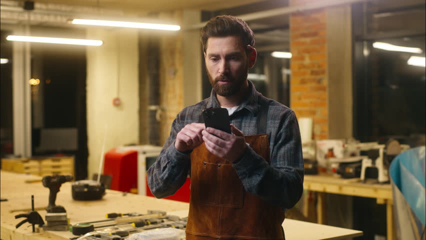 Amazed Caucasian wood master repairman man guy male scroll mobile phone surprise online shocked handyman saying workman wow emotion in workshop builder worker winning carpenter celebrating excitement