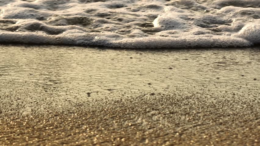 A close-up of the golden beach and foamy waves rolling in, with the soft light reflecting on the water, evoking a sense of calm and tranquility, ideal for beach and nature themes. Thailand.