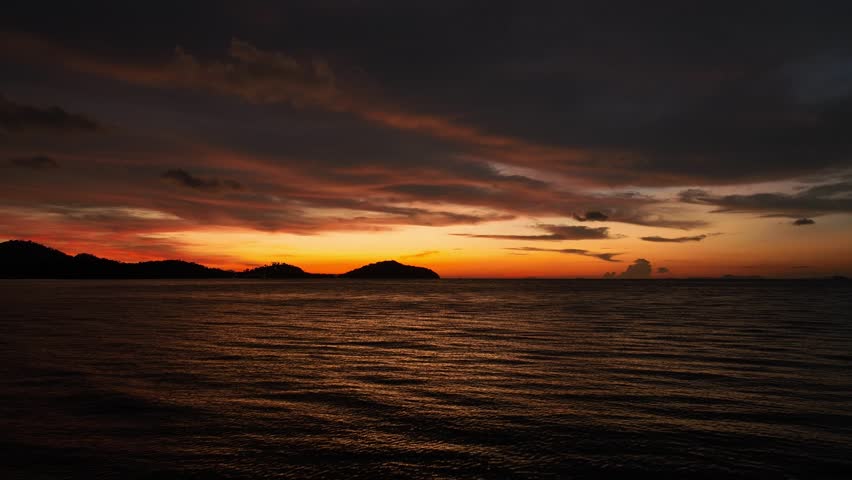 A captivating aerial view of a dramatic sunset over the ocean, with the glowing sky reflecting on the water and distant islands silhouetted against the vibrant colors. Phuket, Thailand.
