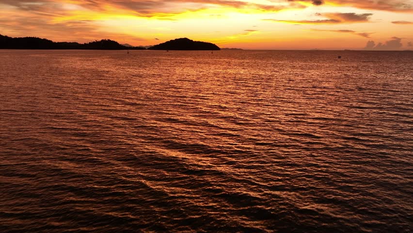 A sunset over the ocean, with vibrant golden and purple tones blending in the sky, and the calm waves reflecting the colors, offering a serene and picturesque view of the coastal landscape. Thailand.
