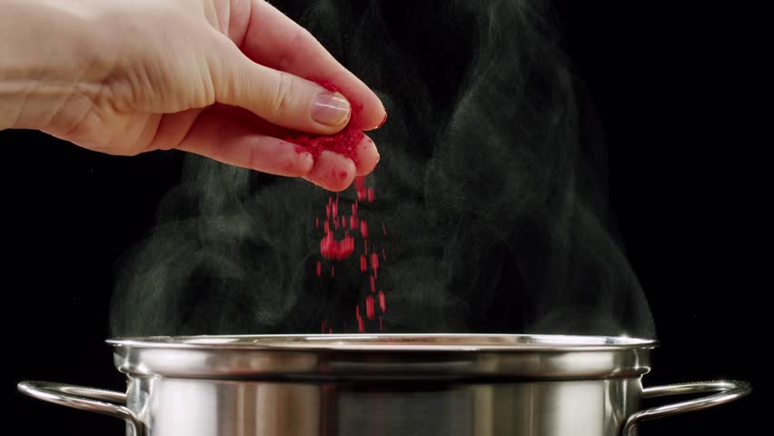 Professional chef adds paprika fragrant dry peppers to a pot of boiling food. Restaurant kitchen cooking, colorful spices, dropping spices.