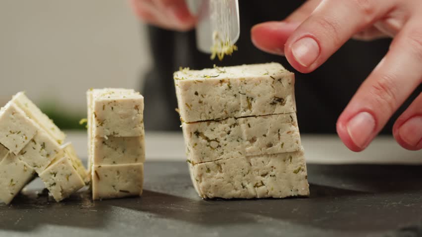 Fried tofu with sesame seeds and spices on cast iron pan, cooking japanese salad. Healthy ingredient for cooking vegan vegetarian diet food. Roasted tofu over black background.