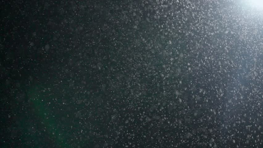 Tiny dust randomly flying in the smoky air, empty space template for objects. Many dust particles white powder falling from above, floating on empty black background in spotlight. Slow motion.