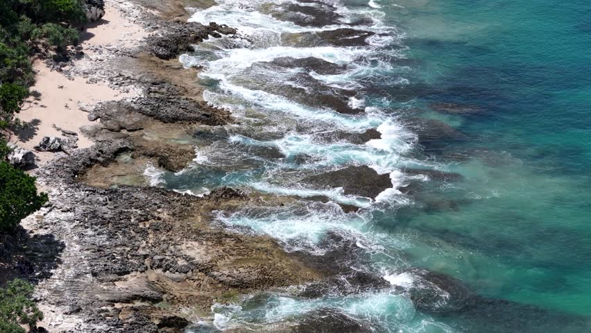 Scenic aerial shot showcasing rocky coastline and foamy waves against turquoise sea.