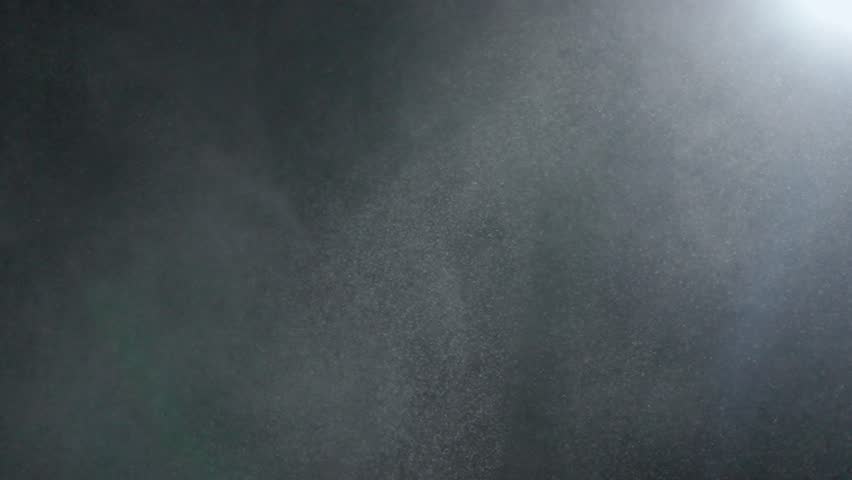 Tiny dust randomly flying in the smoky air, empty space template for objects. Many dust particles white powder floating on empty black contrast background in spotlight. Slow motion.