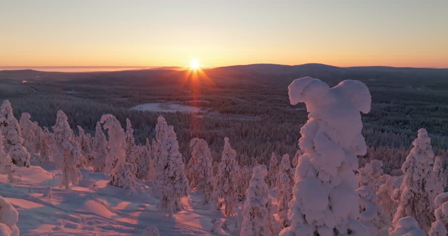 AERIAL: Sunburst above snowy trees and arctic fell mountains, winter in Lapland