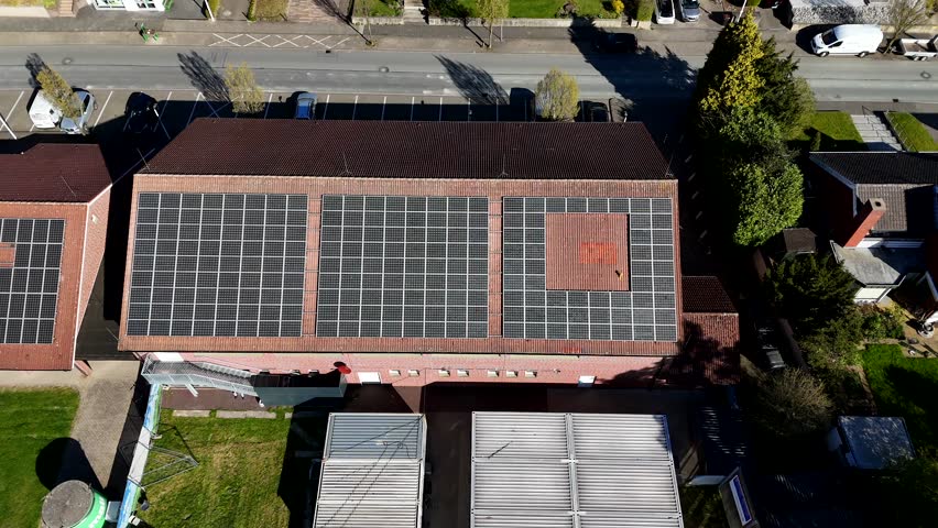 Solar panels on red tile roof of apartment building. Sunny day in spring season with green grass. Aerial top down shot. Renewable energy production during bright sunlight.
