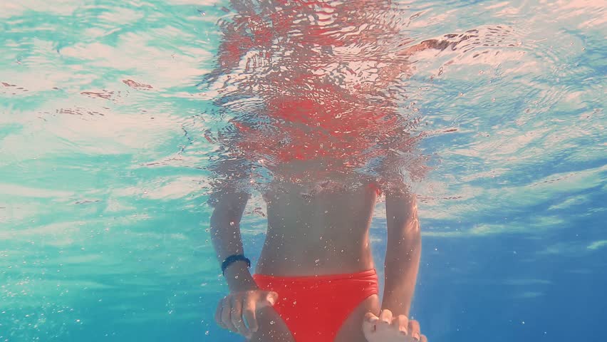 Underwater video sequence capturing young girl swimming, playing, and diving in pool with orange swimsuit and goggles, showcasing summer recreation and childhood joy