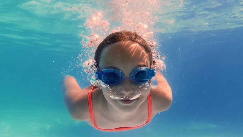 Underwater video sequence capturing young girl swimming, playing, and diving in pool with orange swimsuit and goggles, showcasing summer recreation and childhood joy