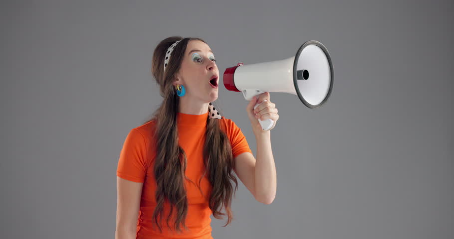 Woman, loudspeaker and shouting in studio with announcement for fashion deal by background space. Person, bullhorn and voice with fist, audio and noise for info, sale or promotion with vintage style