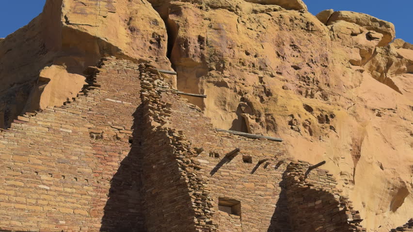 Partial pueblo ruin built into tan sandstone cliffside at Chaco Canyon, New Mexico.