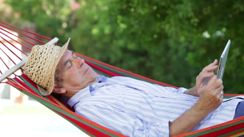 Senior man rocking in hammock using digital tablet. Shot on Canon 5d Mk2 with a frame rate of 30fps