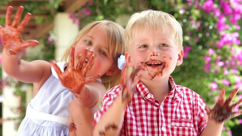Children sitting at table waving chocolate covered hands to camera. Shot on Canon 5d Mk2 with a frame rate of 30fps