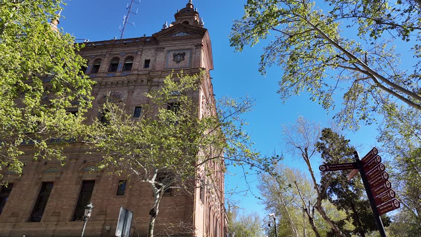 Walking Tourist Turns To Look At The Directory Pointing To Plaza De Espana In Maria Luisa Park In Seville, Spain. Historic Landmarks, Sightseeing, Tourist POV.