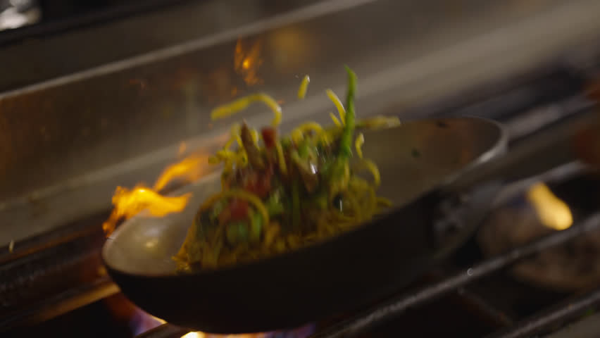 Capturing the dynamic motion of stir-frying vegetables in a flaming wok, showcasing a vigorous culinary technique.