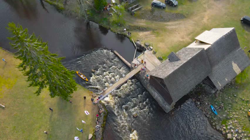 Overhead view of kayak crossing rapids at Võhandu rowing marathon, Estonia. Drone flying above raft paddling through river rapid crossed by small bridge and people watching on riverside, epic journey