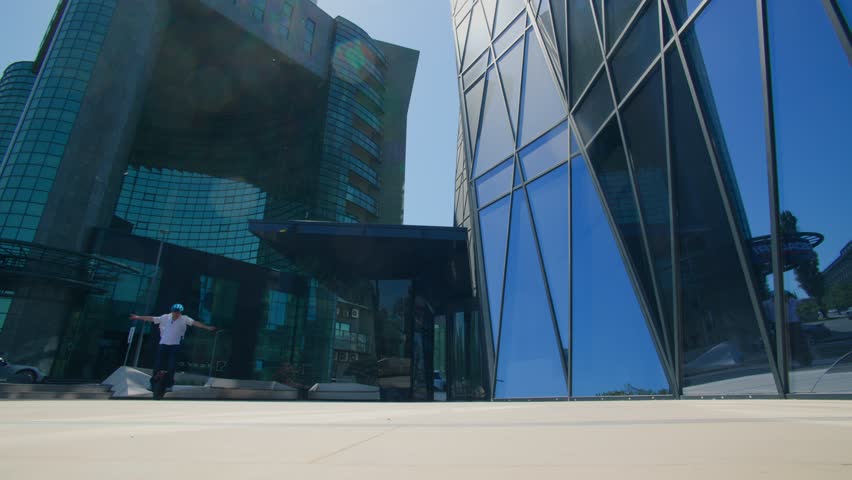 Rear view of a tech-savvy man riding an electric monowheel into the entrance of a glass-fronted office tower, showing off clean energy mobility.
