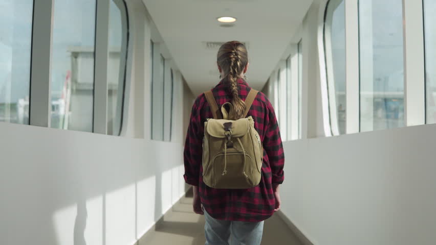 Female tourist with backpack is going along jet bridge to airplane. Woman is boarding to plane using jetwalk connected terminal gate and airplane. Solo trip. Single traveler. Tourism concept.