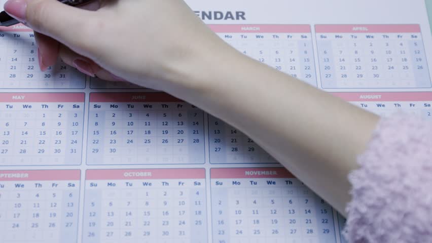Close-up view of someone marking a bold diagonal line on a yearly calendar. This photo emphasizes organization, goal setting, and effective scheduling.