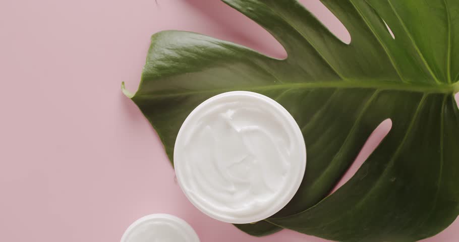 White Jars for cosmetics with tropical leaves Monstera on a pink background in studio.Glossy cosmetic jar with cream.Bottles skin care cream with tropical leaves Monstera for Beauty treatment. Natural