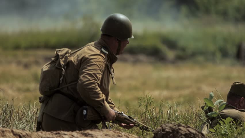 Aged Red Army infantryman sits down in trench and prepares for defense during Great Patriotic War in USSR historical reconstruction. Soviet soldier at combat simulation. WWII recreation battle. Summer