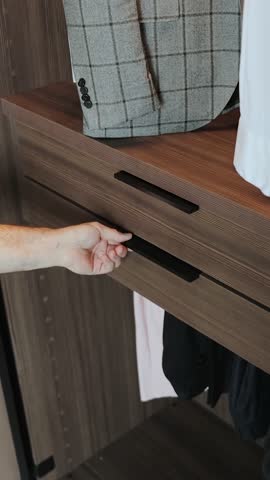 Close-up of a man's hand opening a wardrobe drawer to access neatly folded and organized clothes. Vertical video