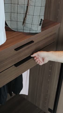 Close-up of a hand opening a wooden drawer in a wardrobe with things, modern interior.Vertical video