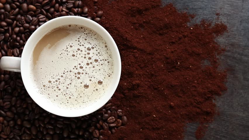 Cappuccino, top view. Cup of cappuccino among coffee beans and ground coffee. Cup of aromatic coffee among roasted coffee beans. Invigorating drink. Copy space