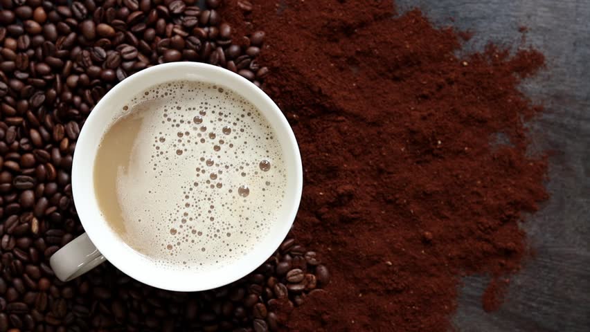 Cappuccino, top view. Cup of cappuccino among coffee beans and ground coffee. Cup of aromatic coffee among roasted coffee beans. Invigorating drink. Copy space