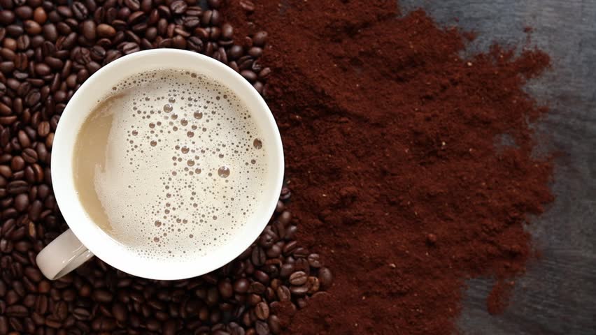 Cappuccino, top view. Cup of cappuccino among coffee beans and ground coffee. Cup of aromatic coffee among roasted coffee beans. Invigorating drink. Copy space