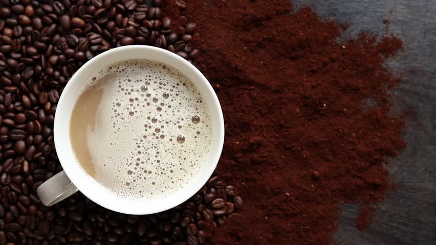 Cappuccino, top view. Cup of cappuccino among coffee beans and ground coffee. Cup of aromatic coffee among roasted coffee beans. Invigorating drink. Copy space