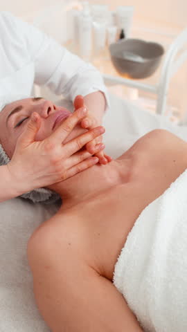 Cosmetologist applying special moisturizing medical cream, scrub, peeling face of pretty Caucasian woman. Facial skin care anti aging cosmetic massage procedure in a beauty salon. Beauty treatment