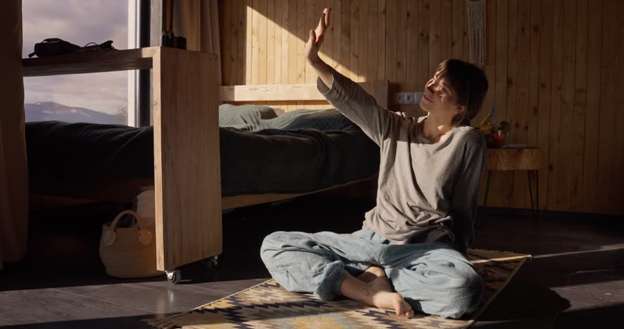 Happy girl playing with sun rays while sitting on carpet after doing yoga in house outside city. Girl enjoys her morning in a quiet house outside the city
