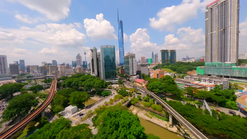 Aerial view of Kuala Lumpur city skyline with skyscrapers, train tracks, and greenery. Urban scene of modern Malaysia showing transport, business, and city life.