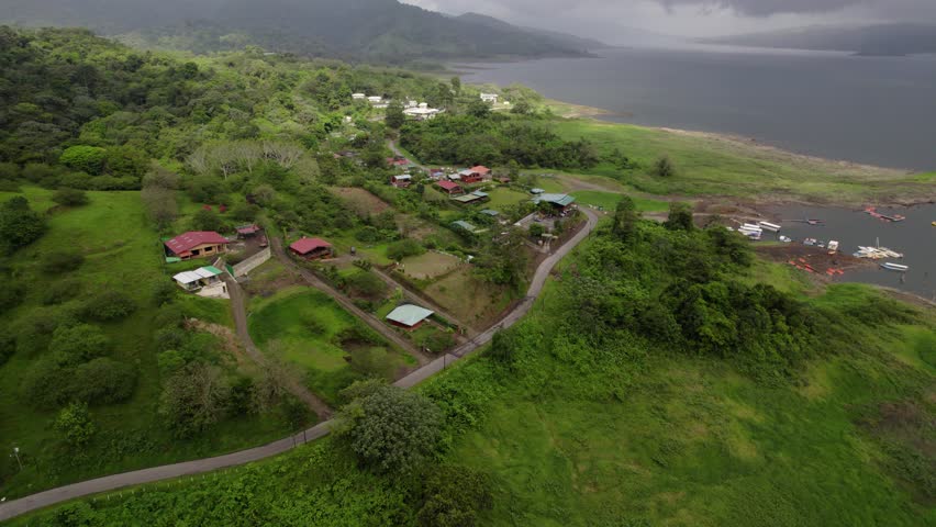 Aerial over El Fosforo lakeside town on Lake Arenal shore tilts up to stormy sky
