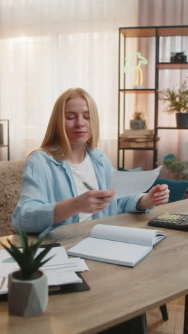 Woman organizes expenses at home, jotting figures into a notebook and verifying papers bills with patience. Caucasian girl at table uses calculator merging clarity and mindful strategy for finance